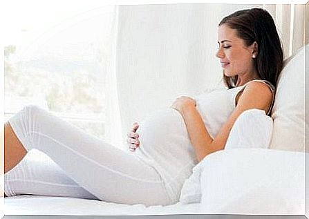 The pregnant woman is lying on the bed